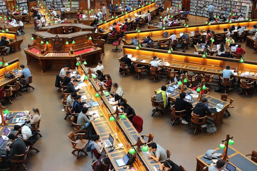 Students working at long tables in a university study hall.