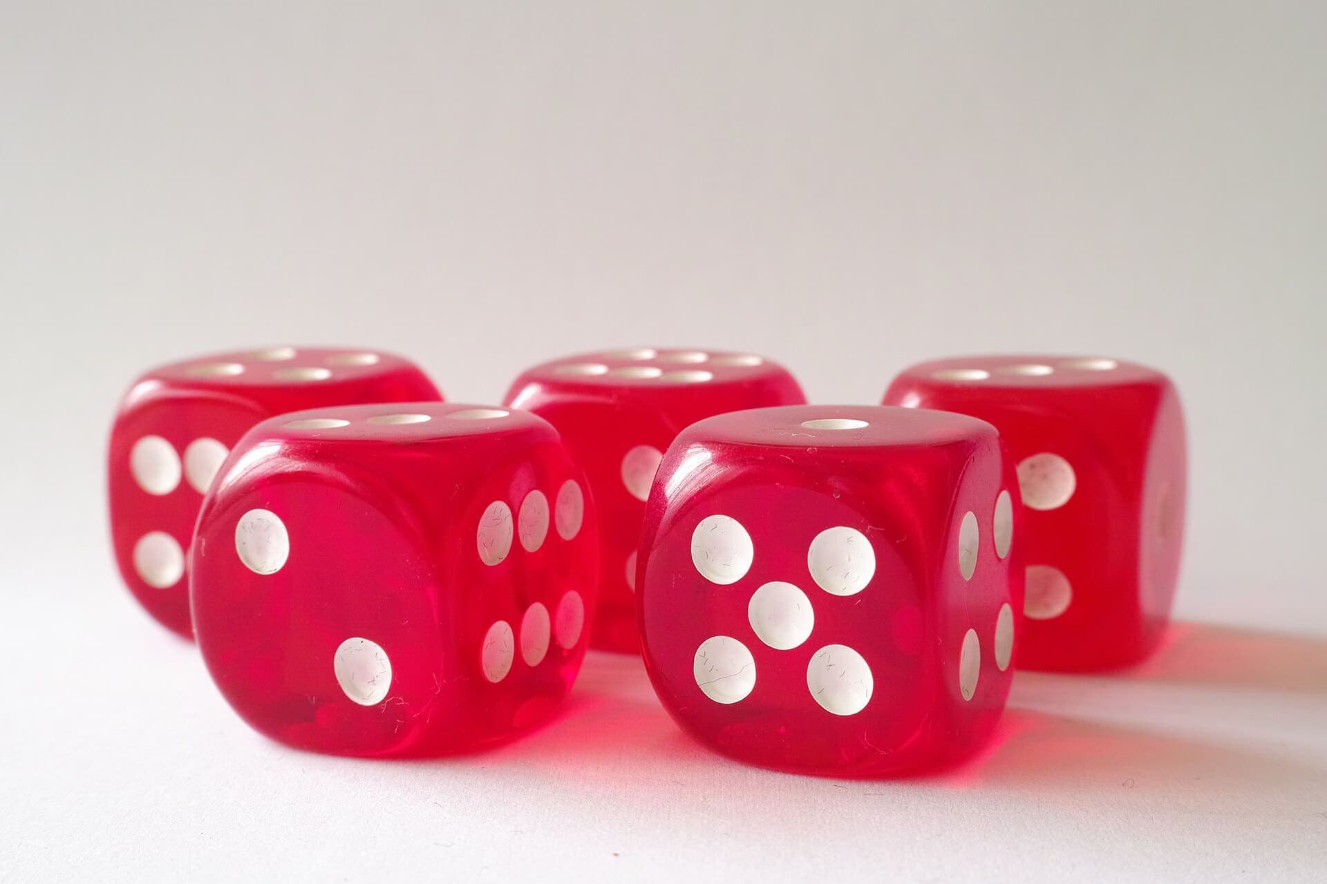 Five translucent red dice with white pips on a white surface.